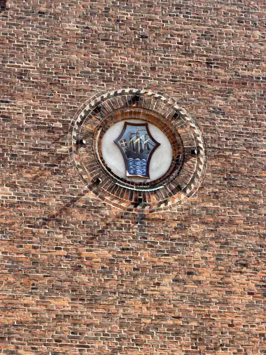 A painted shield depicting a sailing ship above blue waves is set within a circular recess of concentric moulded-brick courses.