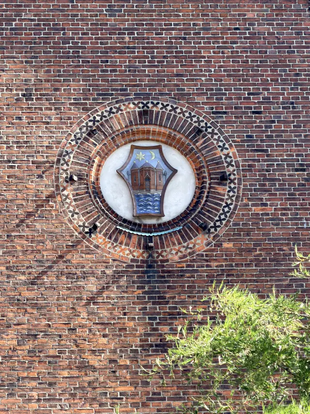A painted heraldic shield of fired clay set in a circular niche of concentric moulded brick.