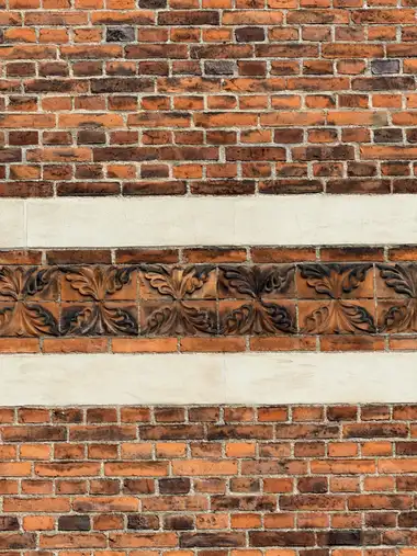 A close view of red brickwork with a horizontal frieze of moulded leaf ornament between pale stone bands.