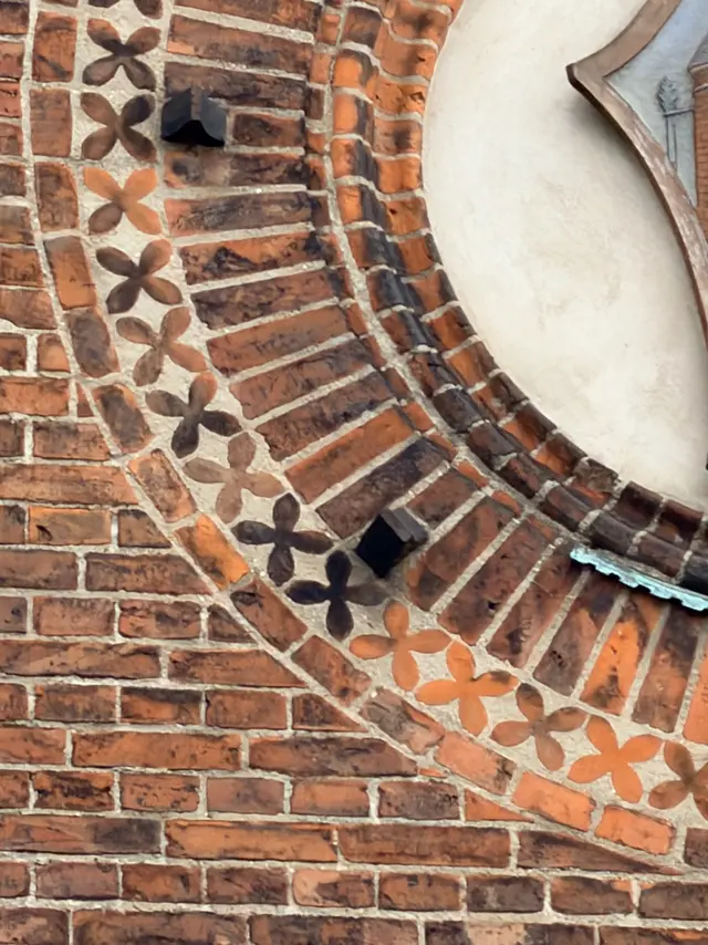 Small moulded flowers repeated along a brick arch, set in pale mortar.