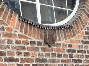 A close view shows radial red-brick masonry around a curved window, with painted glazing bars and a scalloped metal flashing at the sill.