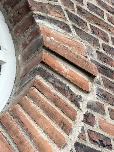 A close oblique view shows projecting moulded red-brick courses beside a white-painted arched opening, with varied firing tones and weathered mortar joints.