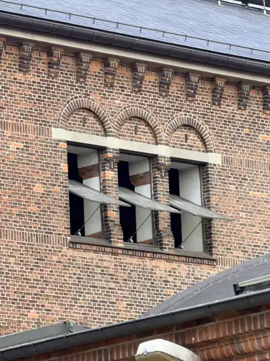 Three tall upper-storey openings with projecting metal awnings sit beneath blind semicircular brick arches and a corbelled eaves course.