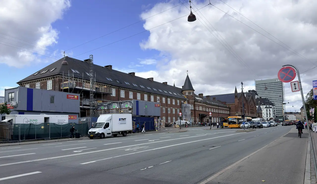 The long brick facade along Bernstorffsgade with slate roof and a corner tower, and hoarding from the works along its base.