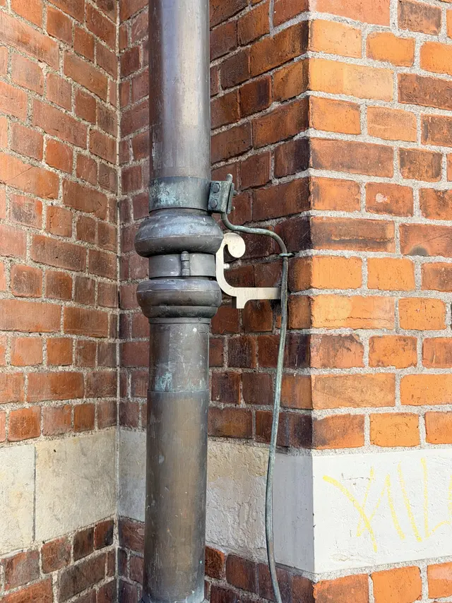 A copper rainwater downpipe and its bracket against brick.
