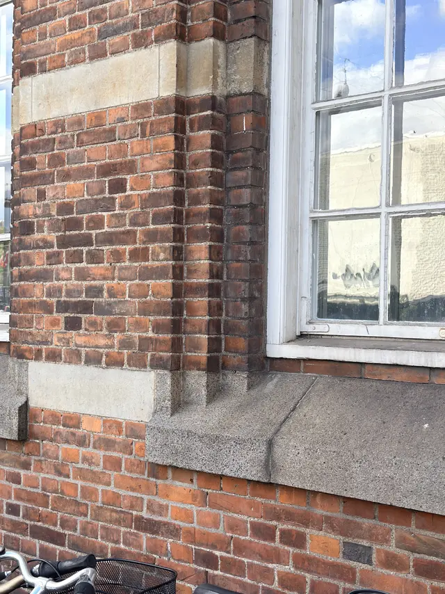 Red brick masonry with a pale stone belt course, a grey stone sill and part of a white-painted timber window.
