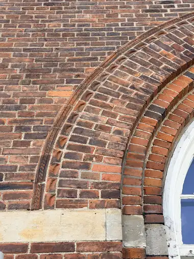 A close view of layered red-brick archwork with moulded bands, recessed ornamental units and several bricks impressed with the cursive date 1908.