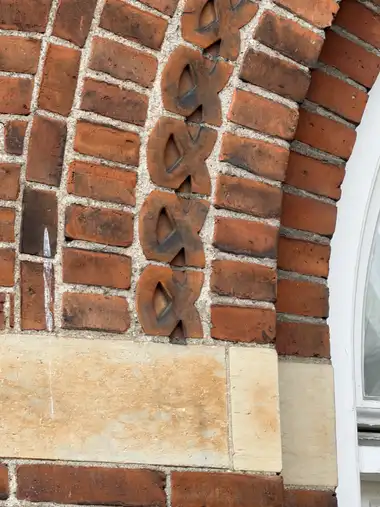 A vertical chain of moulded red-brick ornaments is embedded in common brickwork above a pale sandstone band beside a window.
