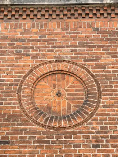 A circular sunburst-like brick medallion with moulded concentric borders is set beneath a projecting openwork brick frieze.
