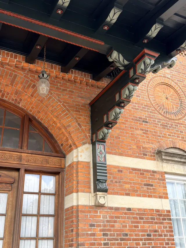 A dark green timber canopy over an arched entrance door, carried on carved brackets, with a glass lantern hanging beneath it.