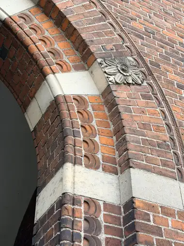Close upward view of a moulded red-brick arch and pier with pale stone banding and a square carved floral relief panel.