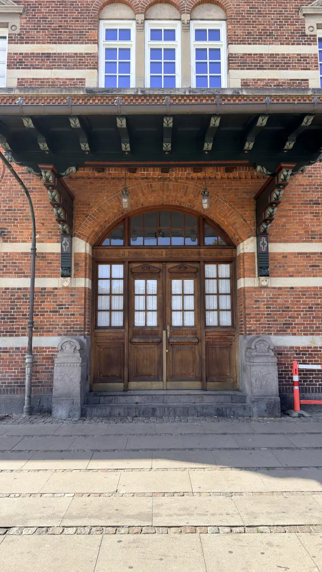 A pair of oak doors with a fanlight above, under a painted timber canopy, between carved granite piers.
