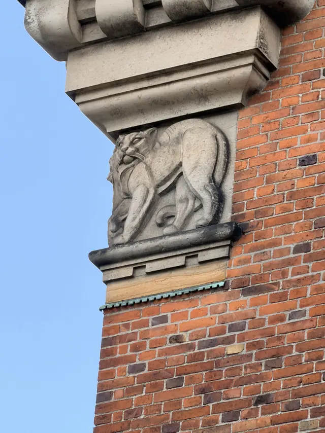 A lean long-tailed carved beast on a bracket beneath the cornice, a serpent held in its jaws.