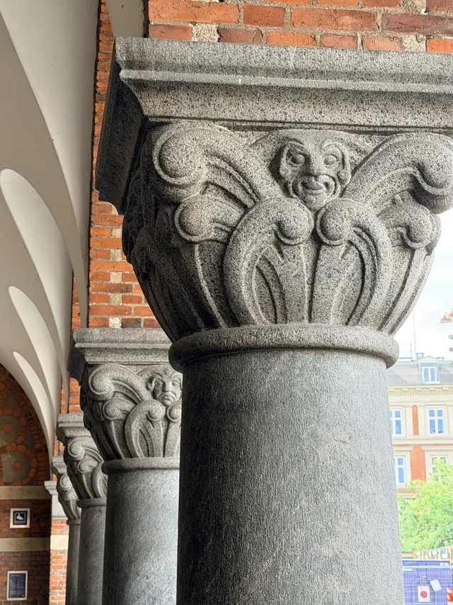 A stone capital on a granite column, with human faces carved among the foliage.