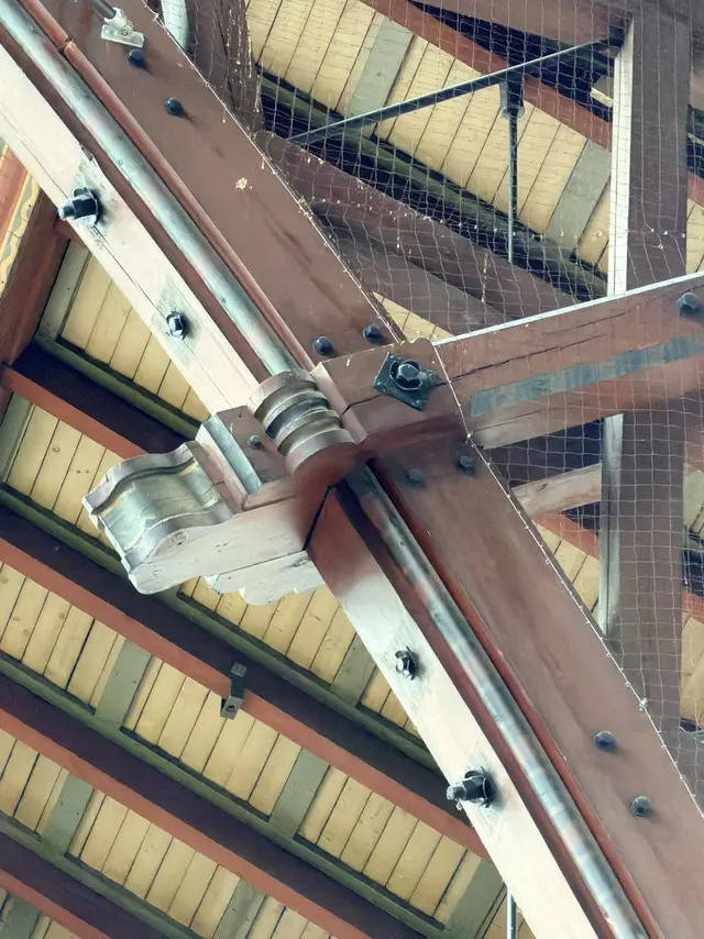 Close upward view of painted timber roof members in the main hall, boards bolted together with iron plates and rods.