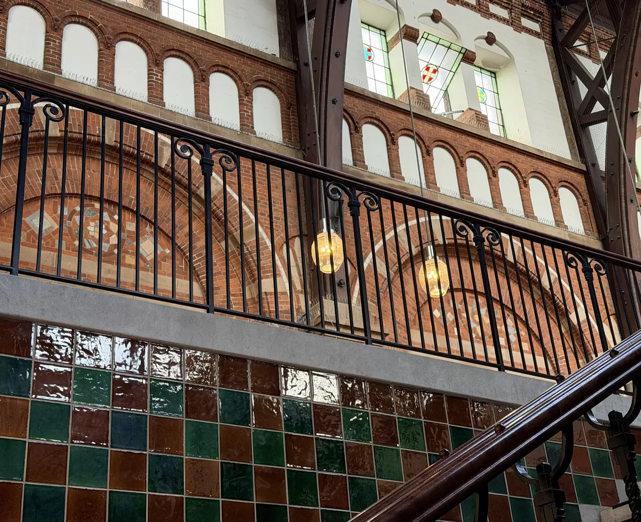 An interior stair with a wrought-iron balustrade, timber handrail and green and brown wall tiles.