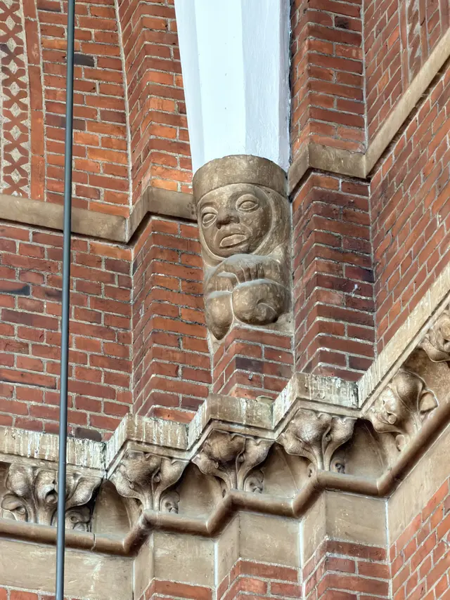 A small human figure in a cap with folded arms, carved on a corner block above a run of leaf corbels.