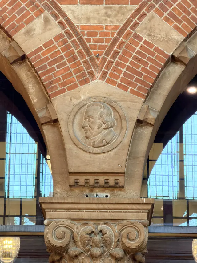 A round portrait medallion of James Watt carved in sandstone where two arches meet above a column.