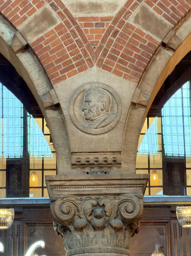 A round portrait medallion of George Stephenson carved in sandstone where two arches meet above a column.