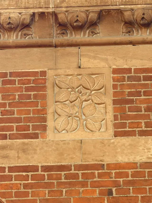 A flat sandstone panel with a spray of broad smooth-edged leaves and small fruits, set flush in the brickwork.