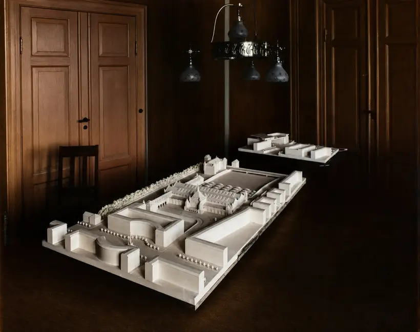 A large white architectural model of a railway complex on a table in a dark panelled room.