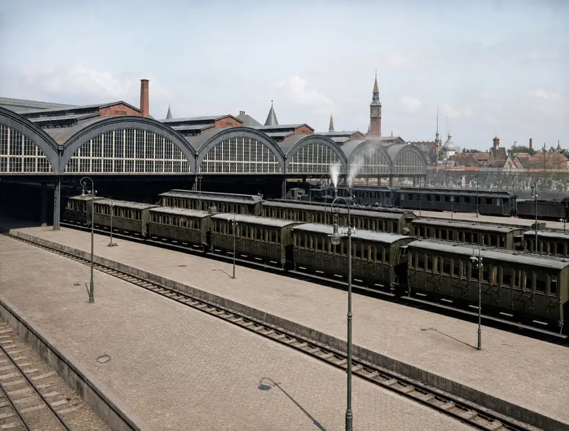 A row of arched glazed gables with dark arch bands, above platforms lined with passenger coaches.