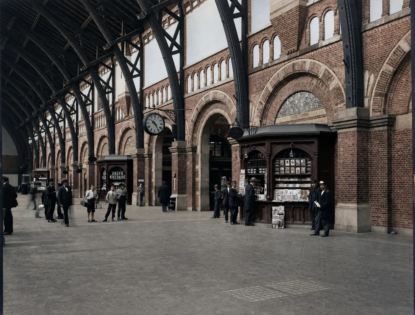 The main hall in use: a tall hall of red brickwork with round-arched openings, an arched timber roof, a large wall clock and a free-standing kiosk on the floor.
