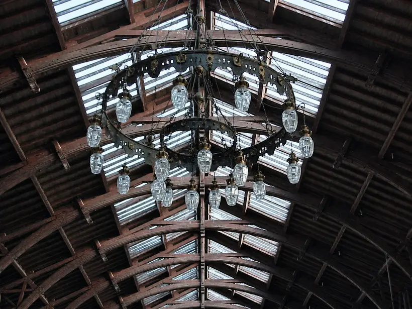 Looking straight up at a curved roof of dark timber. A large two-ring chandelier with many glass lamps hangs on chains beneath it.