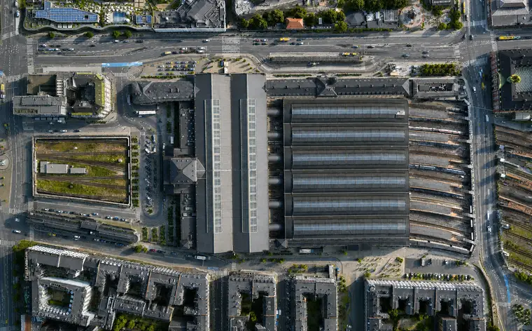 Vertical aerial of Copenhagen Central Station: six curved platform hall roofs side by side, glazing running either side of every ridge, the great hall's roof crossing their north end, the forecourt beyond it and a sunken track cutting held behind retaining walls.