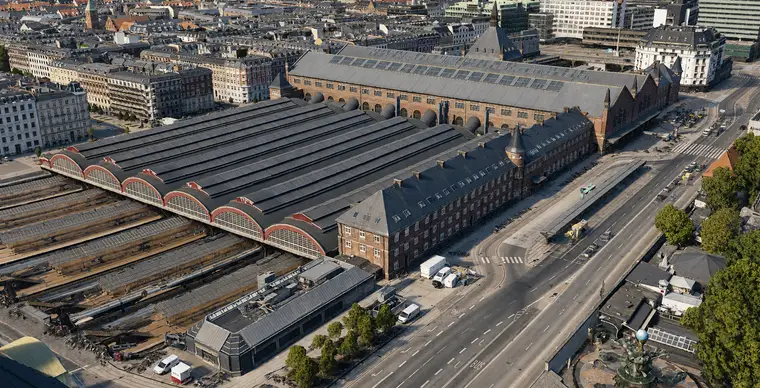 Low aerial of the south ends of the six platform halls: six curved glazed gables in a row, each arch framed in a broad red band on a pale sill course with a small red ridge vent behind its crown, the long dark hall roofs running away behind them and the great hall roof and the north tower's spire beyond.