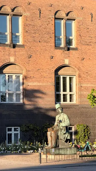 Billede af siddende bronze skriver under udskåret vindue hoveder set fra pladsen, i natursten, tegl, granit og træ.