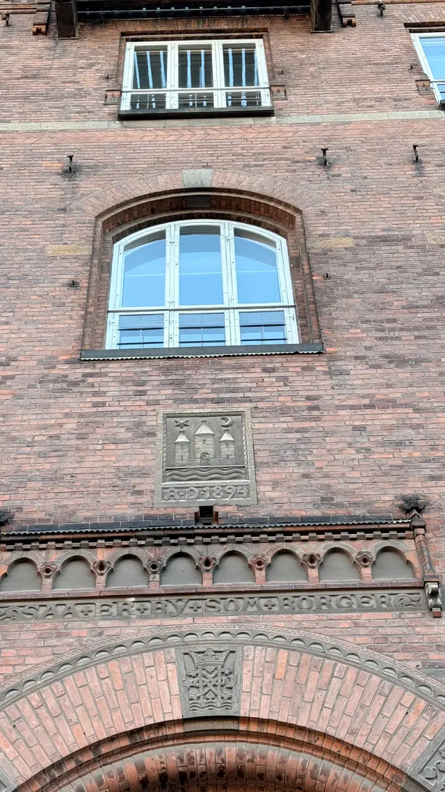 Billede af valgsprog bånd og 1894 våben fra under ved indgangen, i tegl, mørtel, natursten og træ.