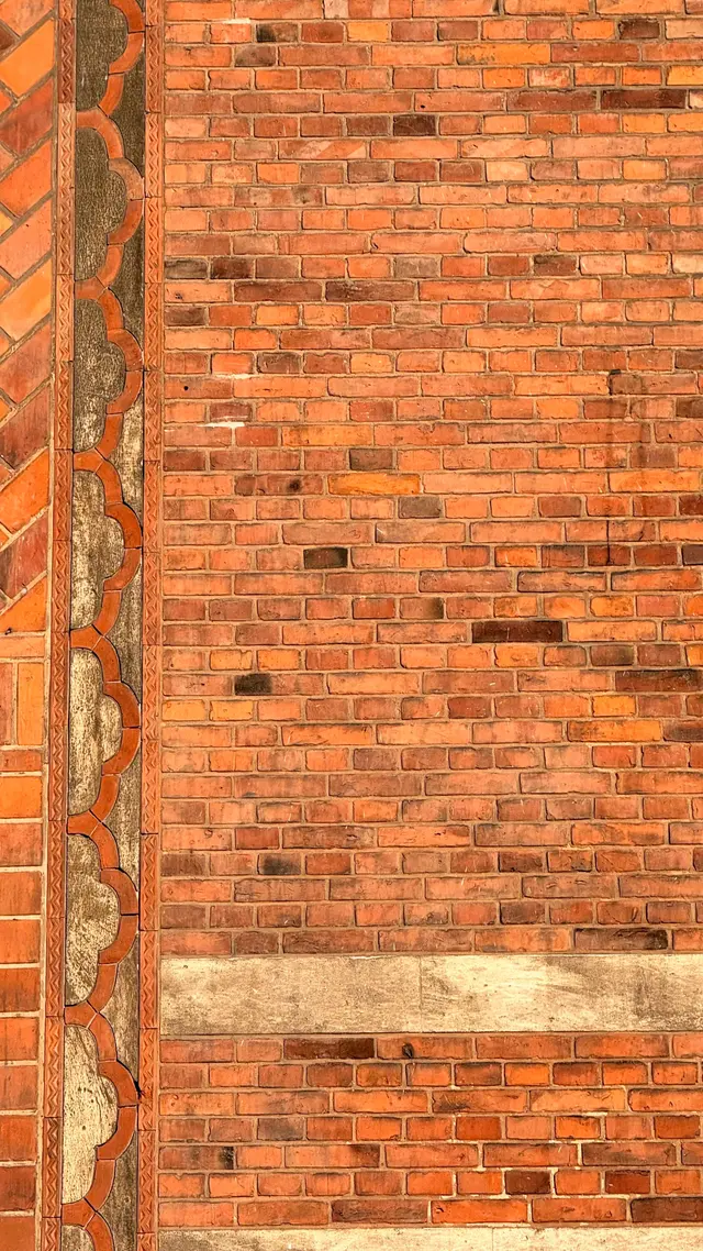 Detaljefoto af profileret tegl zigzag og musling bort på gadefacaden, i tegl, mørtel, sandsten og natursten.