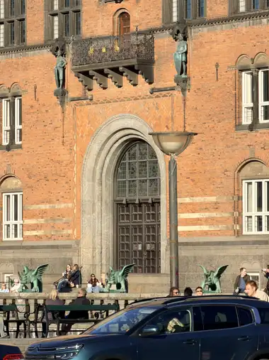 Billede af hoved portal med skjold bærere og altan set fra pladsen, i tegl, granit, træ og glas.