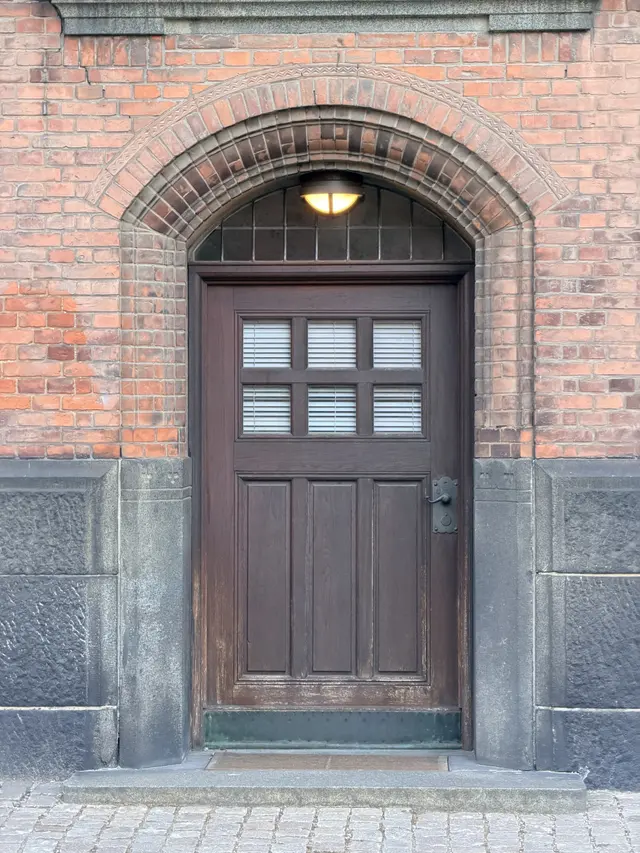 Billede af fyldings træ dør under zigzag bue ved indgangen, i træ, glas, tegl og mørtel.