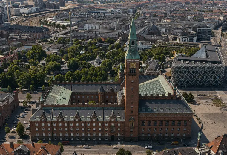 Københavns Rådhus set højt fra øst med hovedfacaden, tårnet, tagene, Rådhuspladsen og Tivoli i København.
