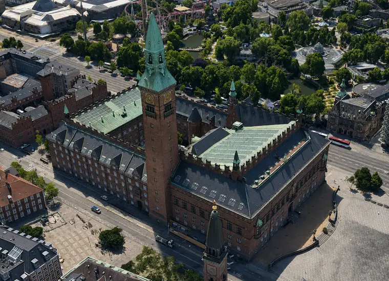 Københavns Rådhus set skråt fra luften med tårnet, gårdrummet, kobbertagene, Rådhuspladsen og Tivoli.