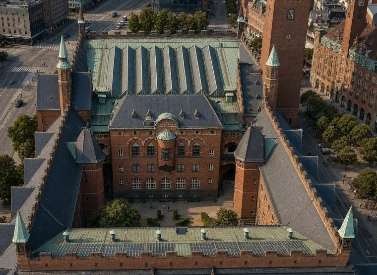 Københavns Rådhus set skråt fra luften med den indre gård, de stejle tage, kobbertagene, hjørnetårnene og det høje rådhustårn i det centrale København.