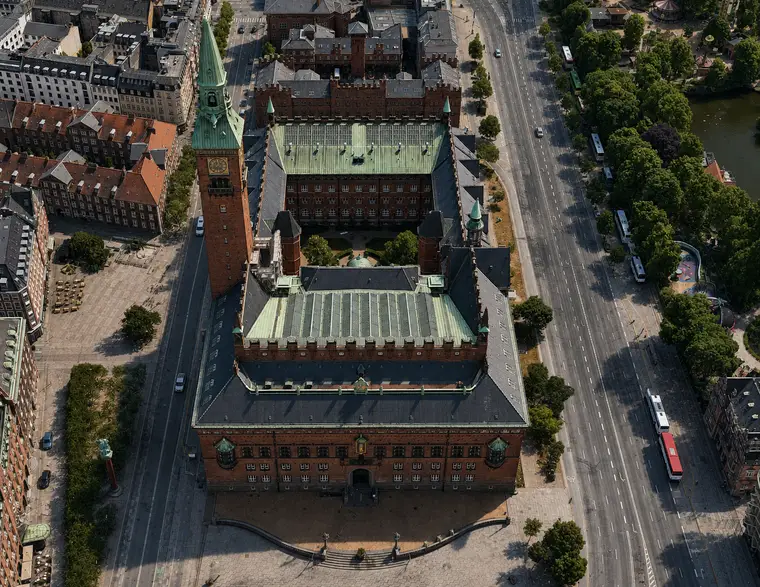 Københavns Rådhus set skråt fra luften med hovedfacade, tårn, gårdrum og kobber- og tegltage omgivet af det centrale København.