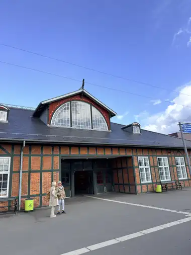 A red-and-green timber-framed entrance gable with a large glazed lunette rises above the slate roof and recessed doorway.