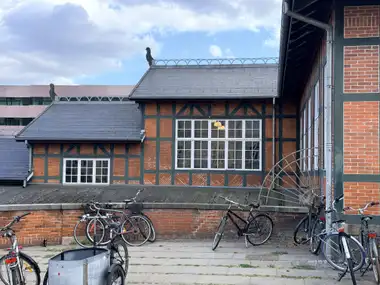 A red-brick and dark-green timber-framed facade with patterned infill panels, white multipane windows, slate roofs, ridge-end animal cut-outs and bicycles along the foreground wall.