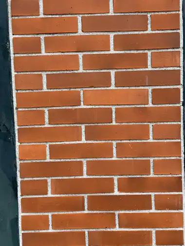 A tightly framed panel of orange-red brickwork with pale mortar beside a dark green-painted timber post.