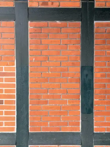 Close view of red brick infill panels framed by dark green-painted timber posts and horizontal beams.