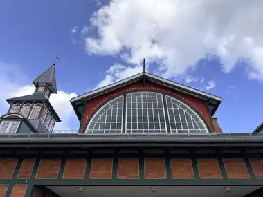 A low-angle view shows the large red-and-green hall gable with its semicircular glazed lunette, alongside part of the clock tower and roofline.