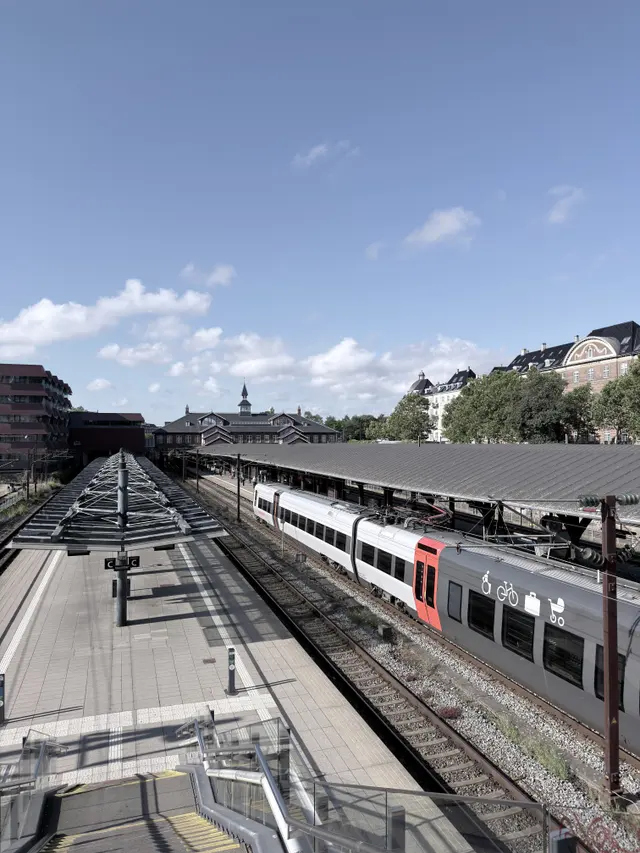 Tracks in a deep cutting below street level, with the station beyond.