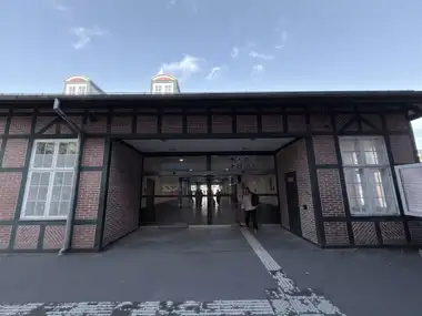 A broad entrance bay is framed by green-painted timber and patterned red-brick infill beneath a deep roof overhang, with glazed doors leading into the station.