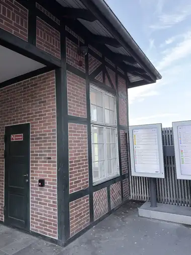 A close exterior bay shows green-painted timber framing with patterned red-brick infill, a tall painted window, and the projecting eaves.