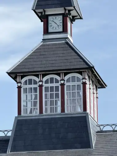 The upper central tower has slate-clad roofs, a glazed timber lantern, red-green-and-white painted woodwork, and a Roman-numeral clock face.