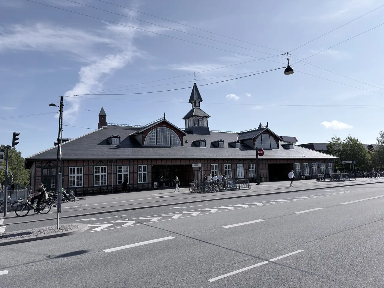 Østerport Station's long street front across Oslo Plads: red brick, green timber, a slate roof, two arched windows and the small clock tower with its spire.