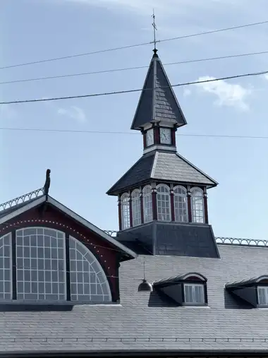 The upper station roof, glazed timber clock tower, steep slate spire and weathervane are framed against the sky.